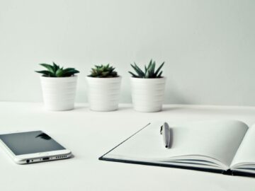 three white ceramic pots with green leaf plants near open notebook with click pen on top