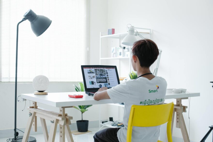 young man in white shirt sitting on chair using laptop